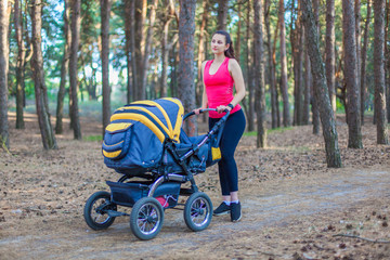 Fototapeta na wymiar Nature walk with stroller, young active mother in sportswear walking on the forest walkway with her baby in the pram, enjoying fresh air