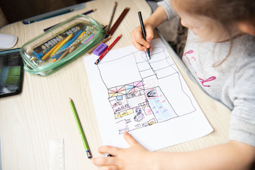 Child drawing plan of the apartment sitting at table at home. Home education. Architectural lesson.