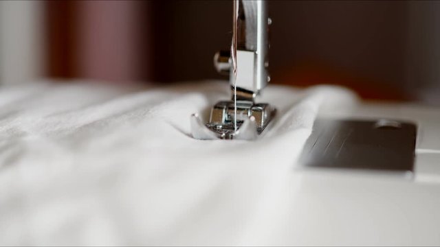Sewing machine sews white fabric with white thread. Slow action, the needle of the sewing machine stitches the fabric. Master class working on a typewriter