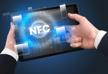 Close-up of a hand holding tablet with NFC abbreviation, modern technology concept