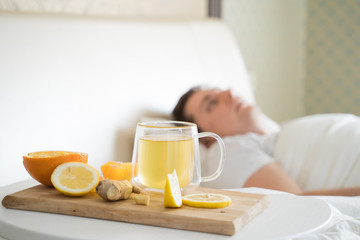 Cup with antipyretic drugs for colds,flu.Sick man in bed. Tea with citrus vitamin C,ginger root,lemon,orange.Wooden tray. Home self-treatment.Medical quarantine antiviral covid-19 coronavirus therapy