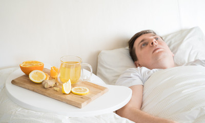 Cup with antipyretic drugs for colds,flu.Sick man in bed. Tea with citrus vitamin C,ginger root,lemon,orange.Wooden tray. Home self-treatment.Medical quarantine antiviral covid-19 coronavirus therapy