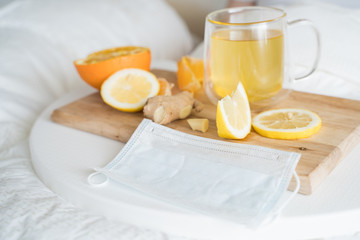 Cup with antipyretic drugs for colds,flu.Sick man in bed. Tea with citrus vitamin C,ginger root,lemon,orange.Wooden tray. Home self-treatment.Medical quarantine antiviral covid-19 coronavirus therapy