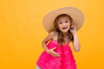 young tourist girl in a summer pink t-shirt with a straw hat on her head on a yellow studio background
