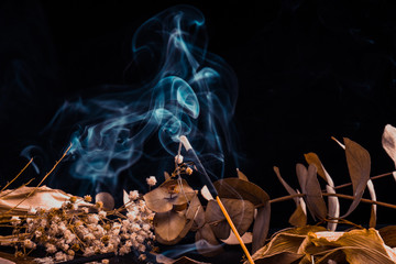 Stick holder and incense stick with leaves and flowers on black background