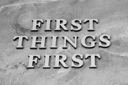 first things first , writen wooden letters on stone background
