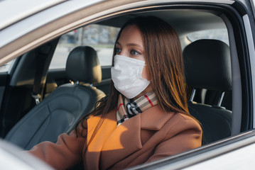 A young girl sits behind the wheel in the car in the mask during the global pandemic and coronavirus. Quarantine