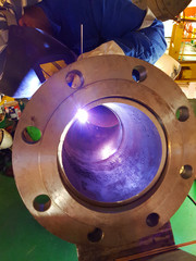 Close up view of welder welding a pipe with flange