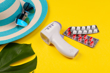Top view on infrared thermometer, white and red pills in blister pack, blue hat, sunglasses,...