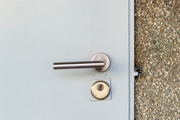 Mortise lock with a knob and keyhole on a metal door painted in gray. Closed entrance from the street to the utility room. Locked door.