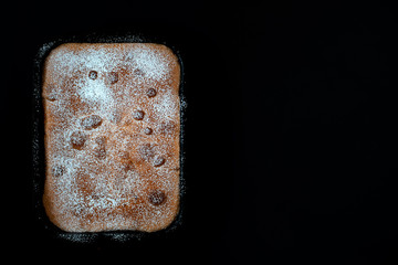 A freshly baked apple pie lies in a metal baking tray. The cake is sprinkled with powdered sugar. Black background . Close-up. Copy space