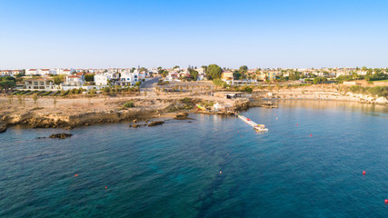 Fototapeta na wymiar Aerial bird's eye view of Kapparis beach, Protaras, Paralimni, Famagusta, Cyprus. Famous tourist attraction Kaparis bay with boats, sunbeds, restaurant, water sports, people swimming in sea from above