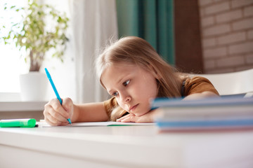 A beautiful girl writes with a pen in a notebook. The child performs homework. Home training, online training