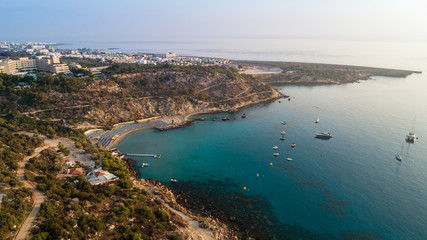 Aerial bird's eye view of Konnos beach, Cavo Greco Protaras, Paralimni, Famagusta, Cyprus. Famous tourist attraction golden sandy bay with boats, yachts in the sea, sunbeds, water sports, from above.