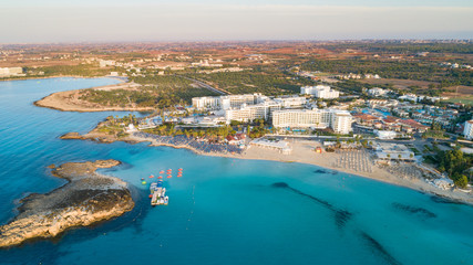 Aerial bird's eye view of famous Nissi beach coastline, Ayia Napa, Famagusta, Cyprus.Landmark tourist attraction islet bay at sunrise with golden sand, sunbeds, sea restaurants in Agia Napa from above