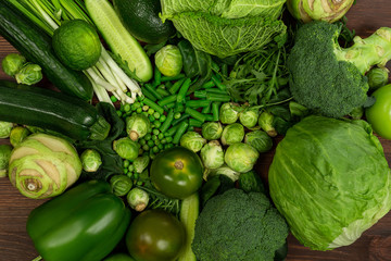 Collection of green vegetables produce on dark background, broccolini, avocado, squash, chilli, grapes part of flat lay overhead set