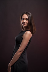Pretty young girl turned around in the darkness. Elegant black dress, so dark everywhere. Amazing girl with attractive appearance