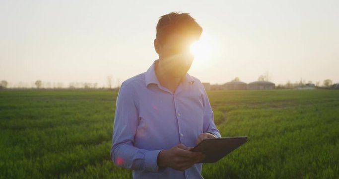 An Agronomist Is Using Technology Tablet For Check And Control The Sprouts Of A Fields And Smiling In Camera Satisfied With His Work. Concept: Innovation, Technology, Agriculture Tech, Career People