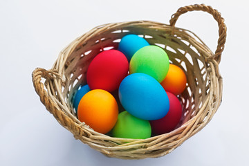 Vibrant multicolored Easter eggs in a wicker basket on a white background
