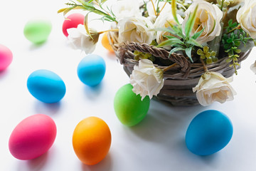 Vibrant multicolored Easter eggs on a white background with wicker basket with white flowers
