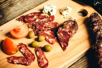 chopped dried sausage and meat with olives and tomato on a wooden board close-up