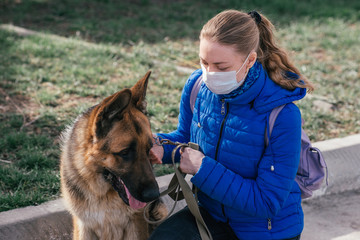 A girl in a protective medical mask walks a dog on the street. Leisure with a pet during...