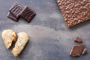Top view of different types of chocolates and crushed gingerbread heart. Chocolate sweets on marble table background.