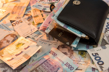 The thick money-laden black men's wallet lies against the backdrop of Ukrainian hryvnia money.
