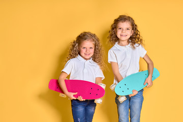 Two Active and happy girls with curly hair having fun with penny board, smiling face stand skateboard. Penny board cute skateboard for girls. Lets ride. Girl with penny board yellow background.