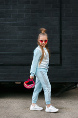 Little girl child wearing a sunglasses and backpack standing in over city background