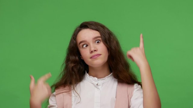 Funny comical teenage brunette girl in white shirt making silly face with eyes crossed, gesturing I'm brainless and crazy, looking with stupid expression. studio shot isolated on green background