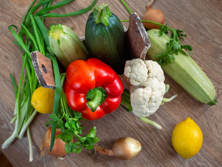 Rustic background with vegetables. Zucchini, bell pepper, and cauliflower are placed in a box with handles. Around the box are also vegetables.