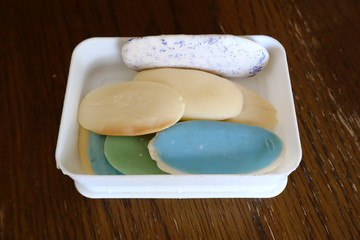Different soaps and remnants in white plastic box on wooden table lot of solid soap for hygiene and cleanliness.close up, top view 