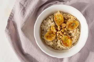 Oatmeal porridge in a bowl with baked bananas, honey and nuts. Healthy vegetarian or vegan breakfast. Copy space, top view. 