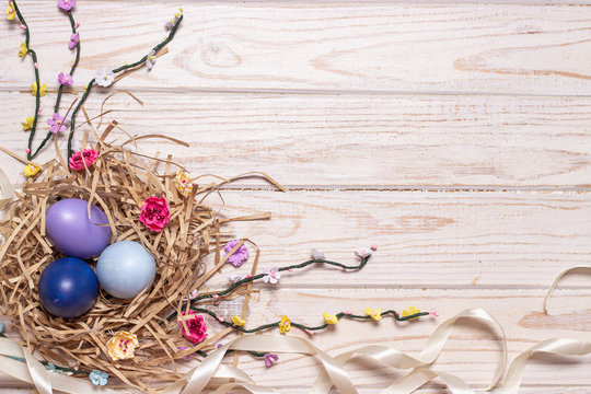 Easter light wooden background with colored eggs in a nest