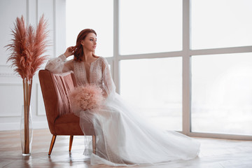 red-haired girl in a white dress sitting on a pink armchair in a bright room
