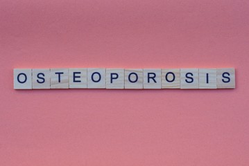 word osteoporosis from small gray wooden letters lies on a red background