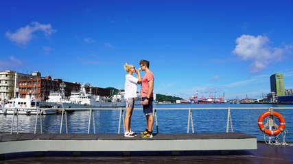 Pretty young European couple, handsome guy and beautiful girl on sunny day have a rest on the embankment in port against the background of ships and boats. emotions joy love happiness. relationship