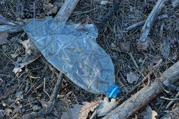 garbage from a piece of an old plastic bottle lies on gray grass and needles in nature