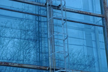 part of a gray iron fire escape on a blue glass wall of a street building
