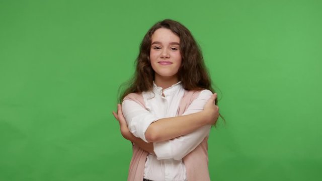 I am beautiful, love myself! Dreamy attractive young brunette girl in white shirt embracing herself and smiling from pleasure, teenage complacency. indoor studio shot isolated on green background