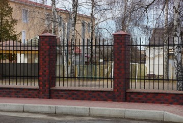 part of the fence wall of black iron bars and red bricks on the street