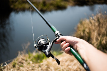 Fisherman holds a fishing rod with a reel in the creek on the fishing