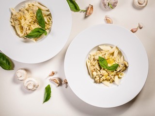 Penne pasta in large white plates with spinach leaves and garlic on a light background. Mediterranean traditional food