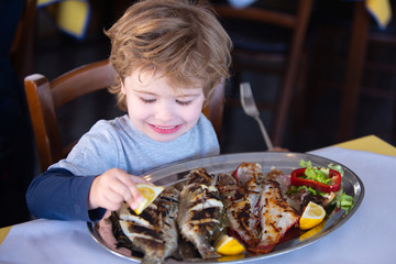 Lemon for fish. Boy pours lemon juice on fish in restaurant. Lunch at the seaside cafe. Seafood for lunch for children. Delicious dinner.