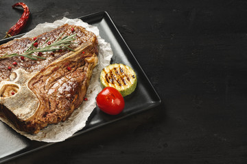 Top view of grilled t-bone steak with spices on black table