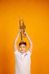 A boy in a white T-shirt holds a trumpet with a musical instrument on his head.