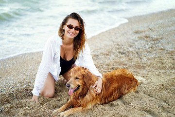 Portrait of happy cute young woman sitting and hugging her dog on the beach.