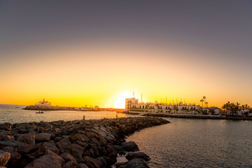 Sunset on the stony coast where fishermen are located during fishing with boats on the horizon and sunlight behind the city buildings from the Grand Canary Island