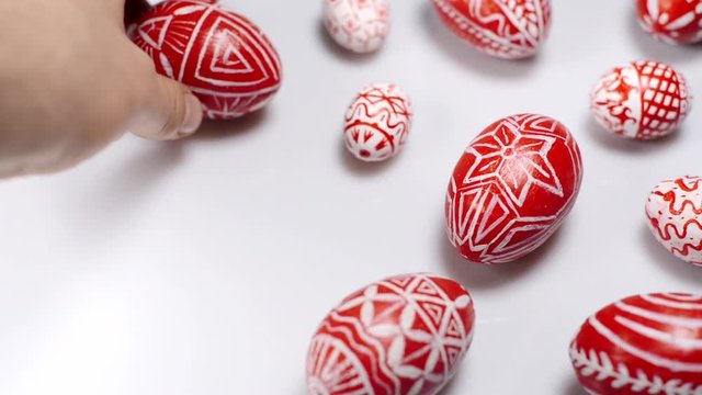 Easter red eggs with folk white pattern lay around on white background. Man's hand add eggs. Ukrainian traditional eggs pisanka and krashanka.
